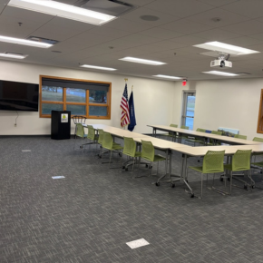 The RCU Community Room, featuring tables, chairs, a podium, a smart TV, and a projector.
